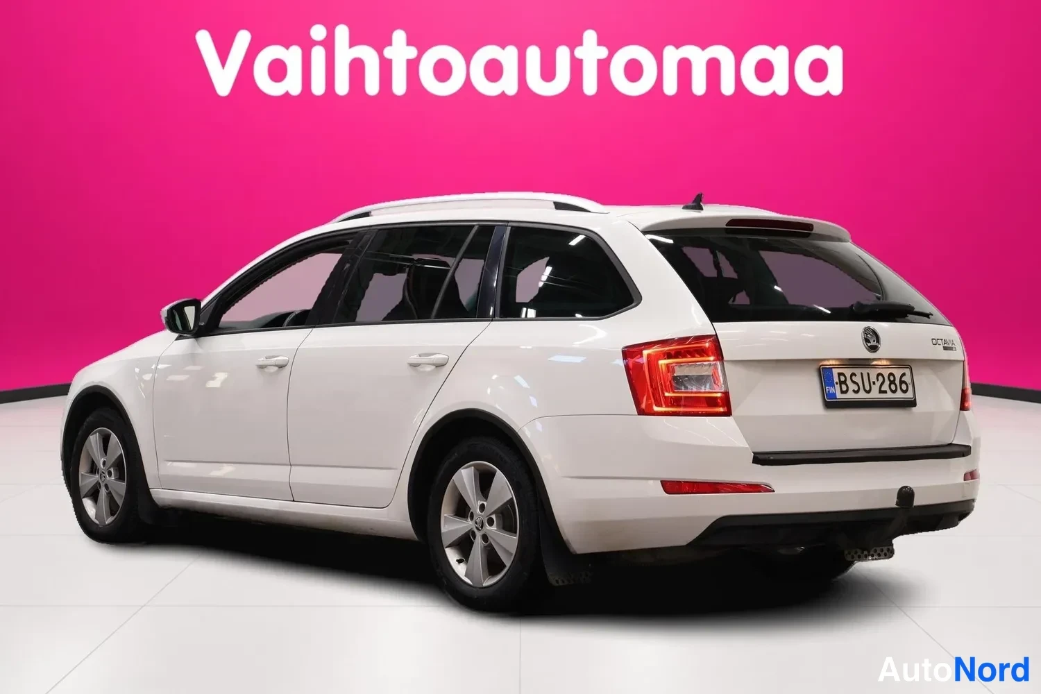 Takaviisto: Valkoinen farmariauto takalokasuunnasta, takavalot ja nokkäön vetokoukku näkyvissä, rekisterikilpi.
