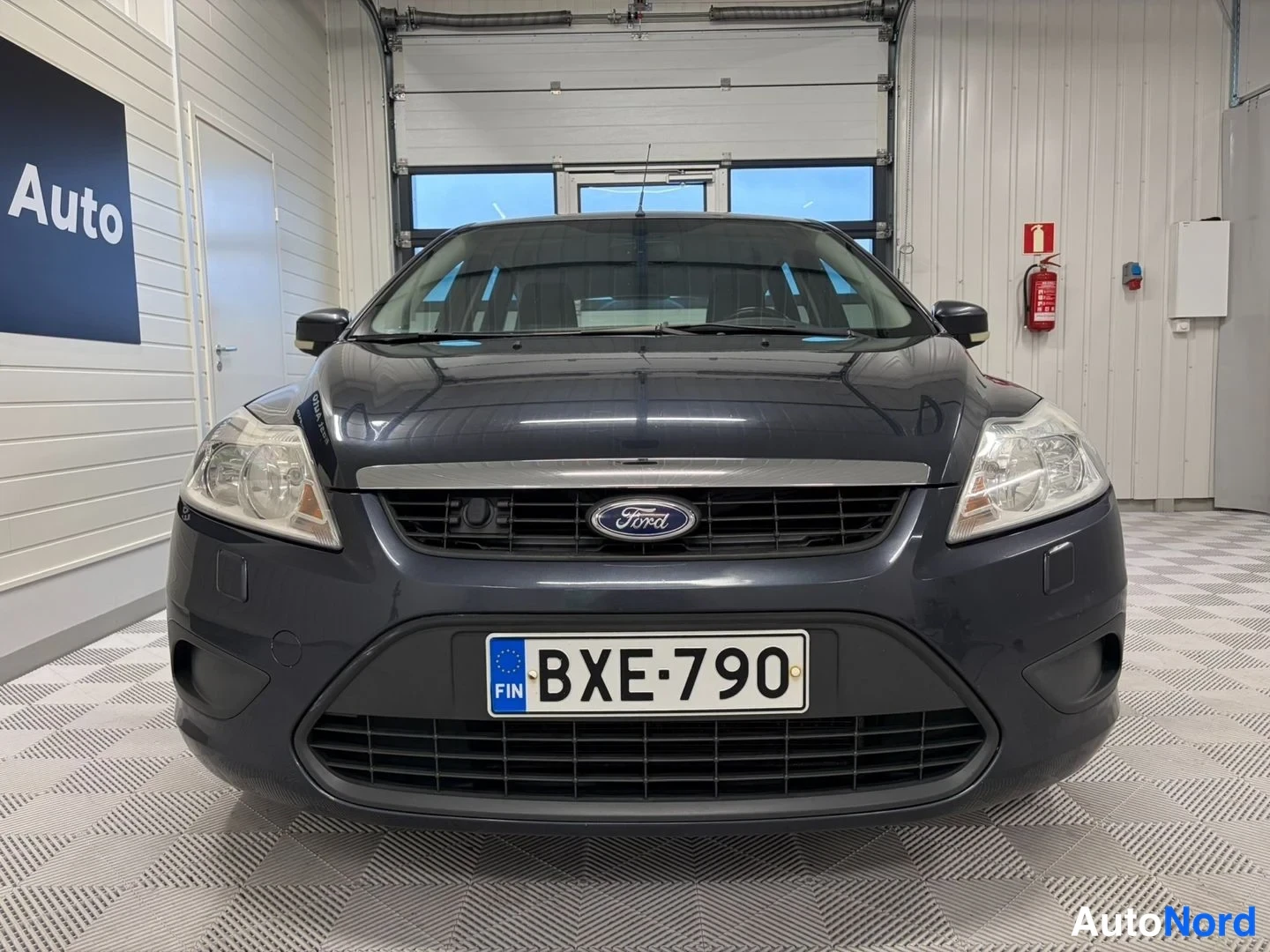 Edestä: Tummanharmaan farmariauton etäosa suoraan edestä kuvattuna, Ford-merkki säleikkössä ja rekisterikilpi.