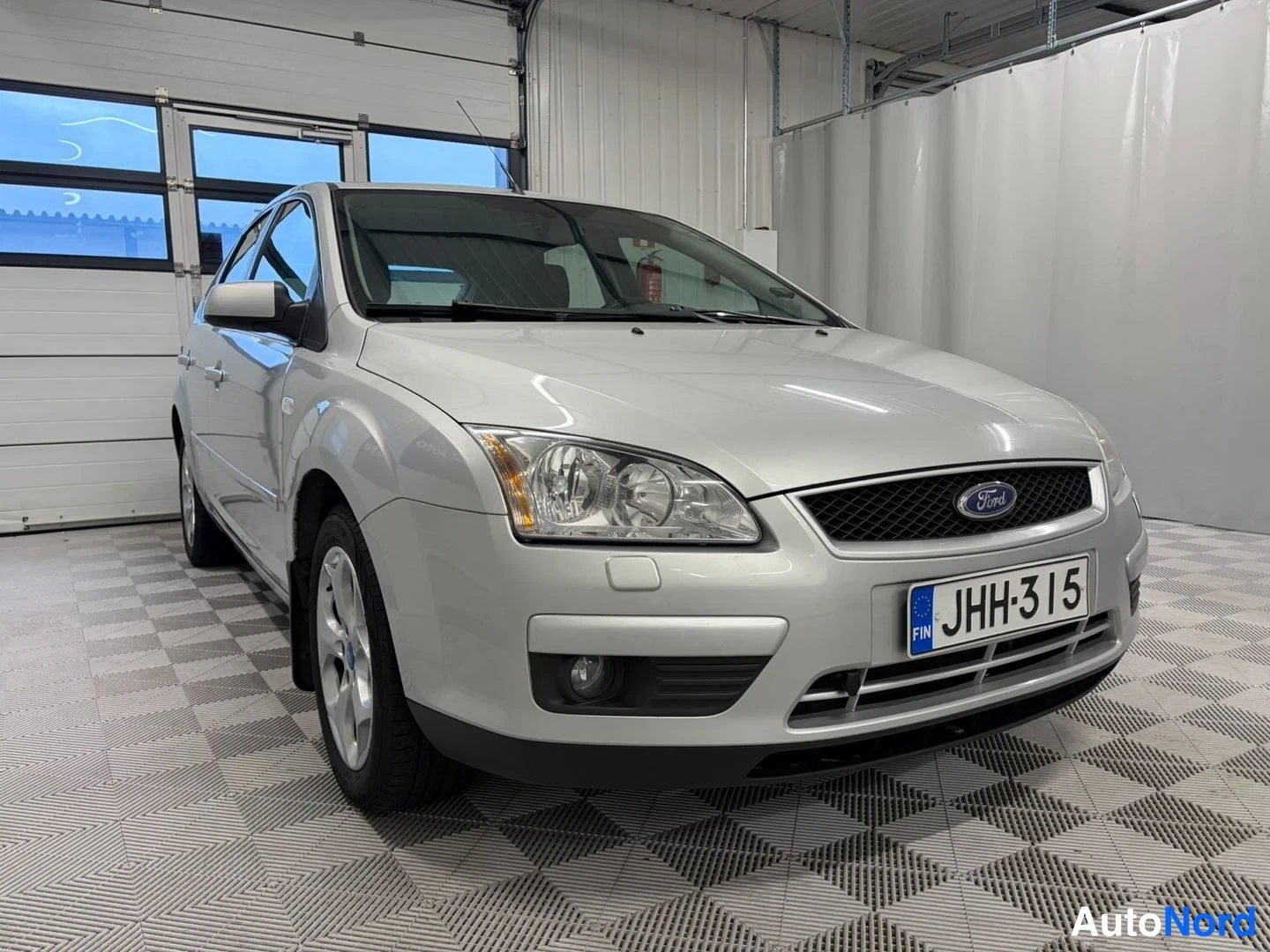 Etuviisto, nokka oikealle: Hopeanvärinen Ford Focus etuosa kolmasosakulmasta, nokka kuvan oikealla puolella, rekisterikilpi.