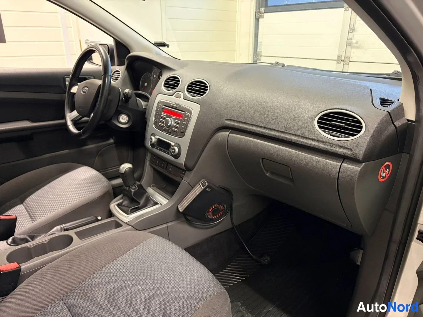 Muu: Ford Focusin sisätilat: ohjaamo näkyy kuljettajan puolelta, manuaalivaihde, radio/CD-yksikkö ja tekstiilimatot.