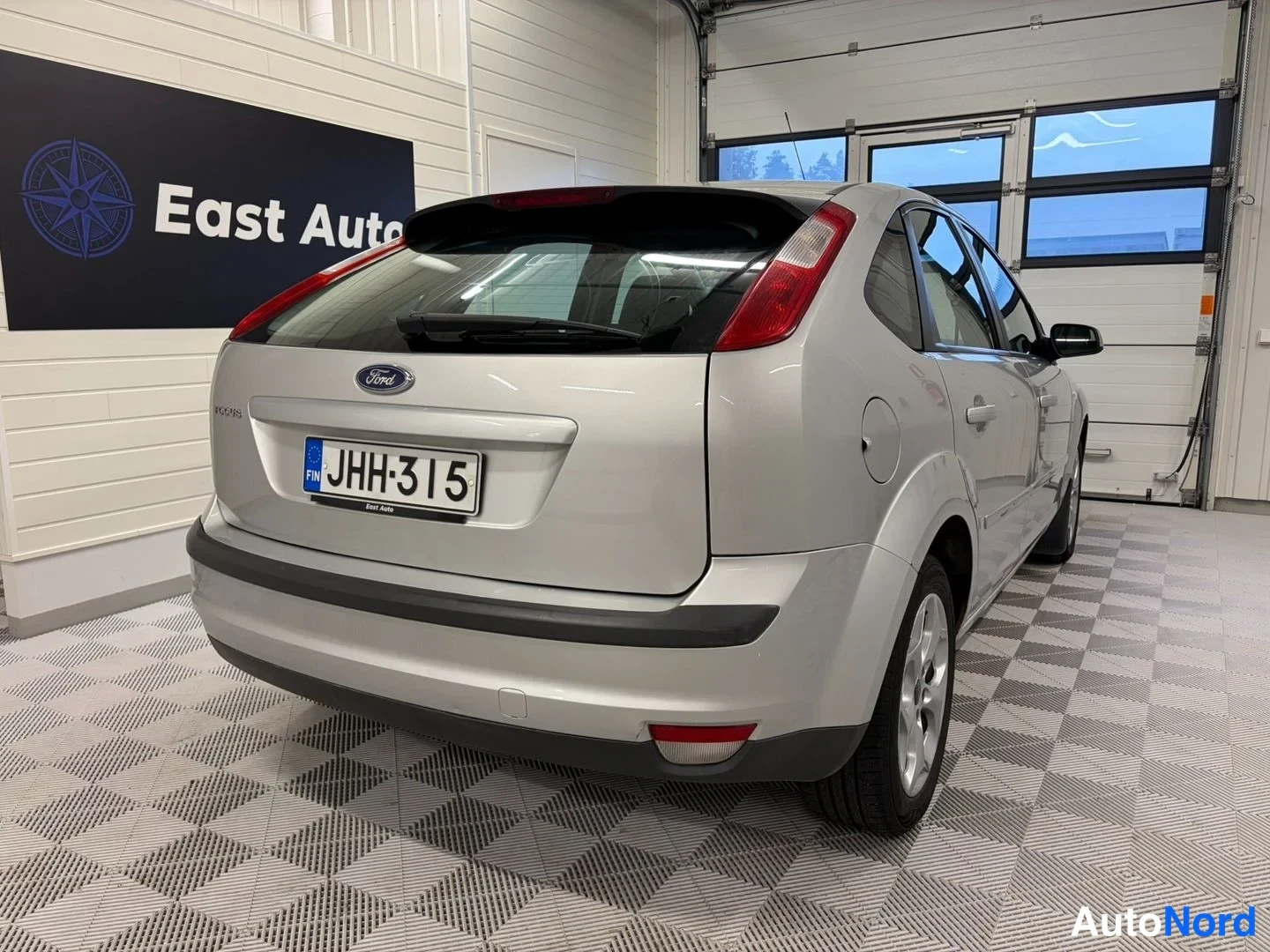 Takaviisto: Ford Focus -farmarin takakulma; hopeaa karbia, kolme ovea näkyvällä vasemmalla sivulla, rekisterikilpi ja Ford-merkki takaluukussa.