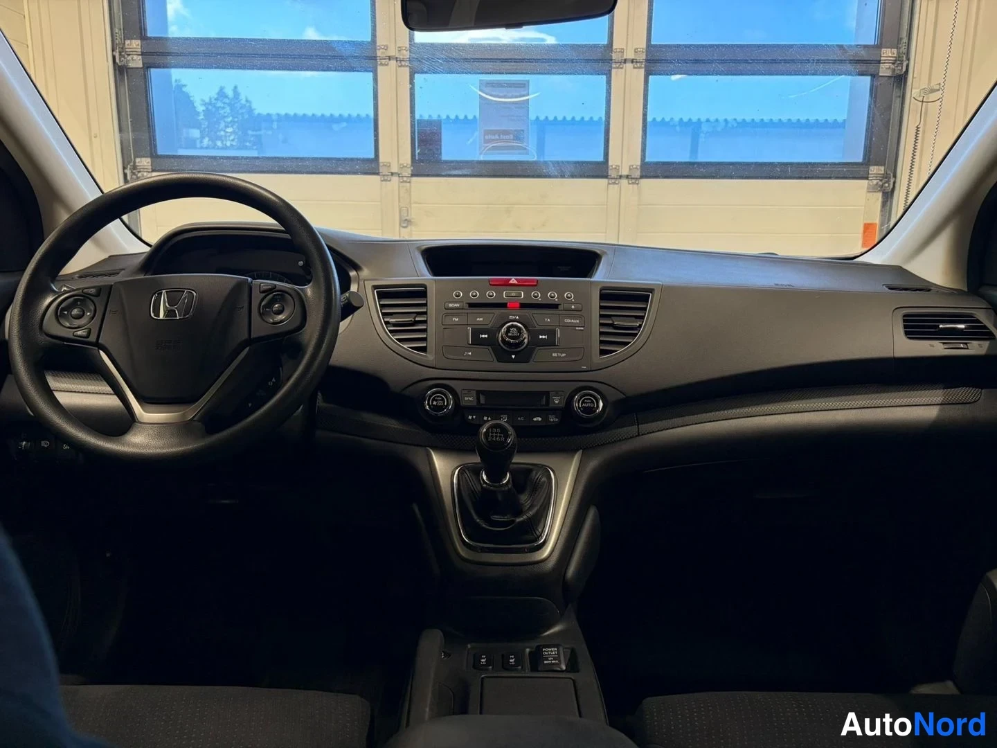 Yksityiskohta: Honda CR-V:n ohjaamo kuvattuna kojelautaan päällä: Honda-merkkinen ohjauspyörä, keskikonsoli, manuaalivaihtolevy ja osin varjostetuksi jäänyt mittaristo.