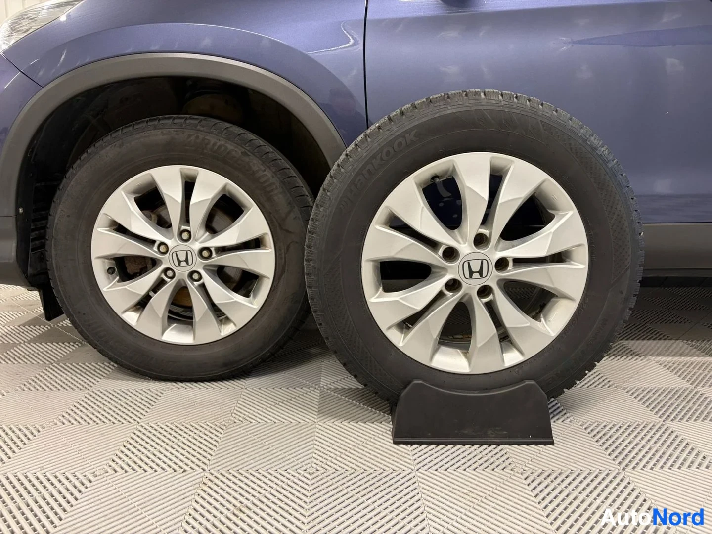 Yksityiskohta: Kaksi Honda-kehävanteen alumiinivanne rengasineen seisseet lattialla, yksi autoon kiinnitettynä ja toinen erikseen esillä.