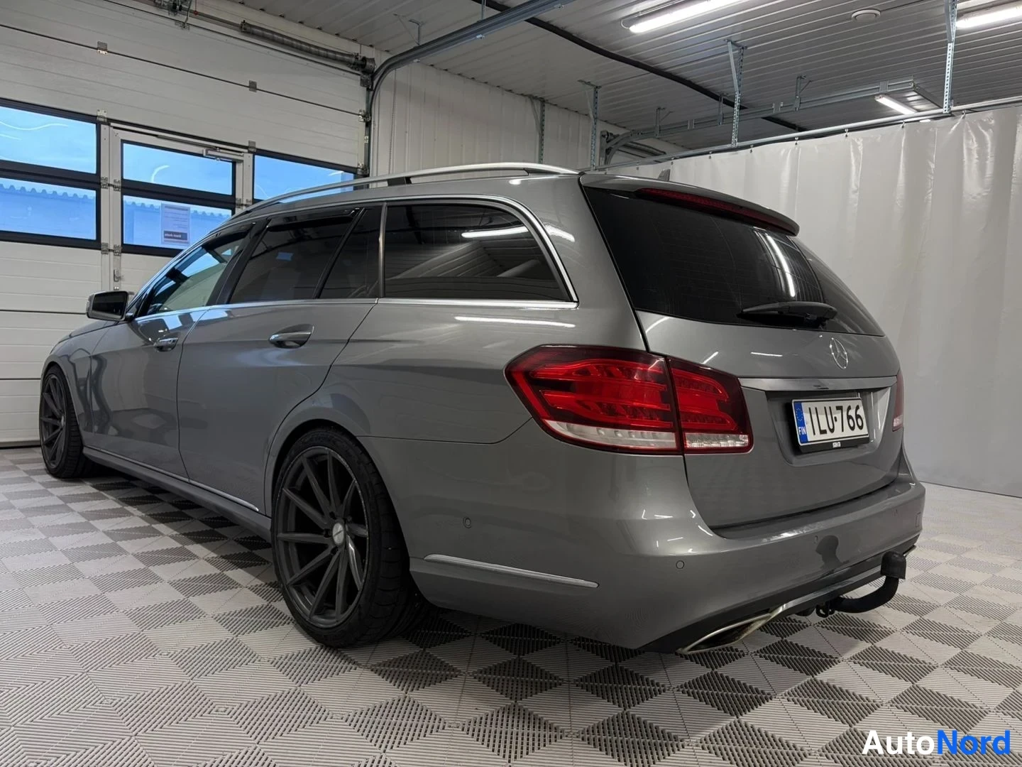 Takaviisto: Mercedes-Benz E-farmari takaviisto katsottiin vasemmalta, harmaa korilla rekisterillä ja mustat vanteet.
