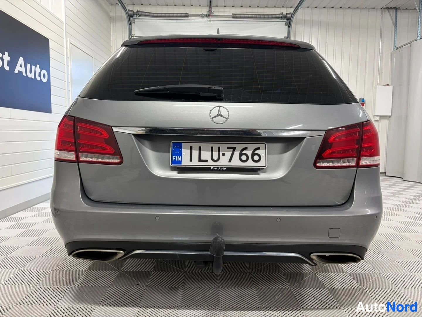 Takaa: Mercedes-Benz E-farmarin takanäkymä, harmaa koria rekisterillä, kaksoispakoputket ja asennettu vetokoukku.