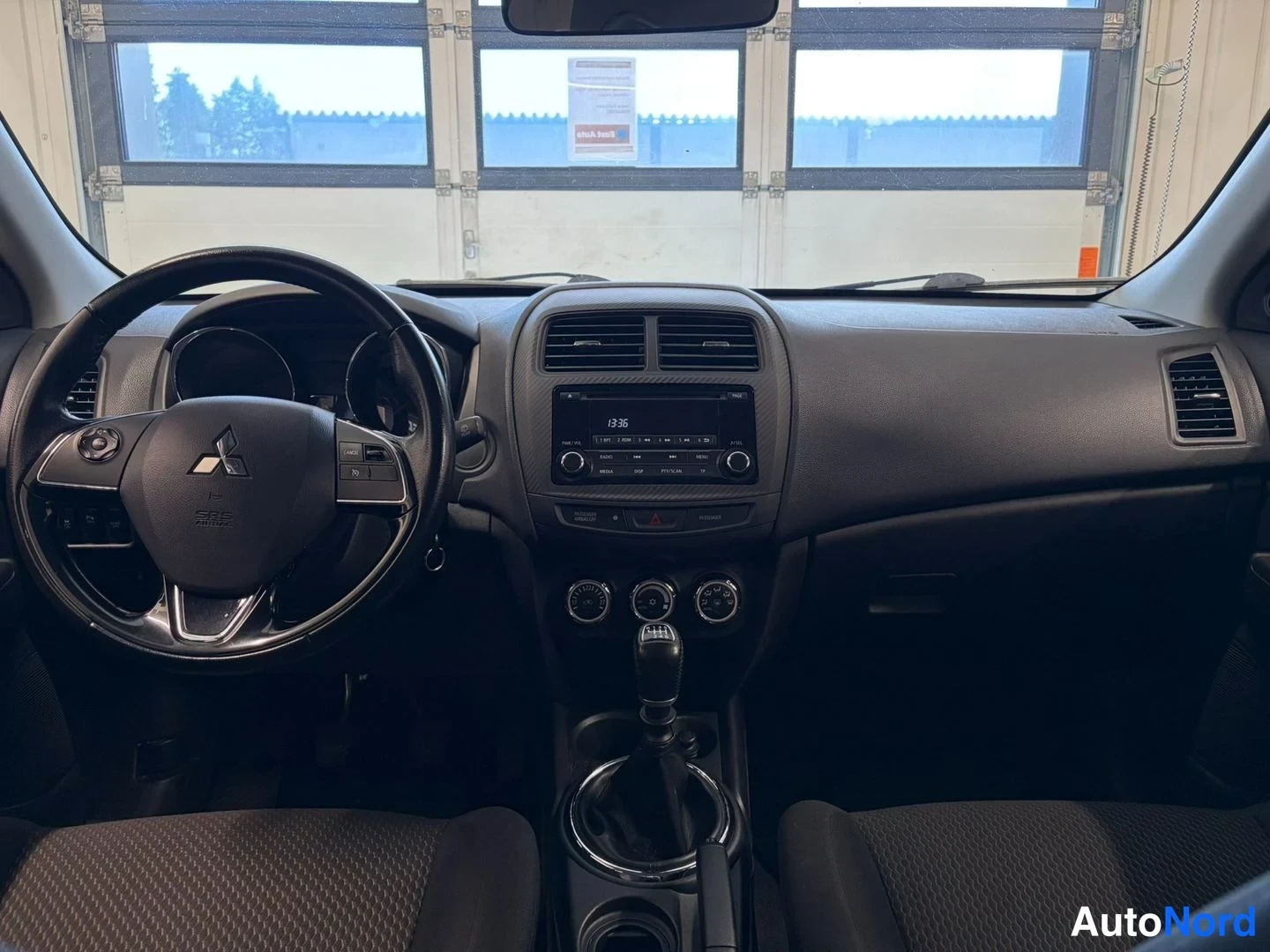 Muu: Kojetaulu suoraan edestä kuvattuna: Mitsubishi-merkitty ohjauspyörä, analogiset mittarit, radio-näyttö ja manuaalivaihteen vipu.
