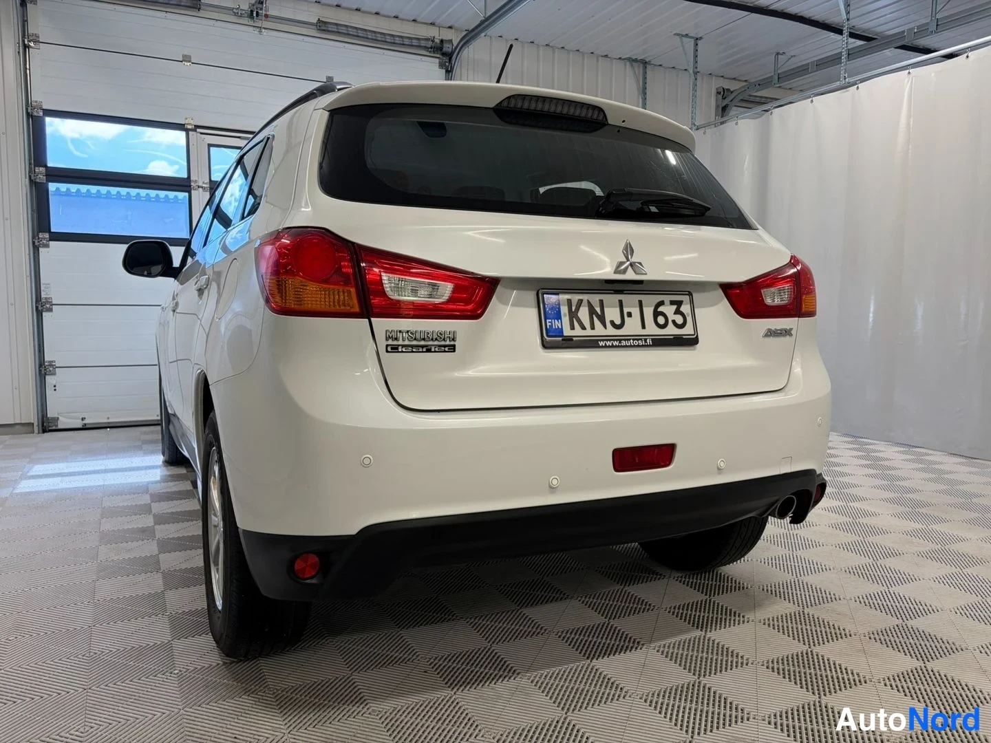 Takaviisto: Valkoinen Mitsubishi ASX farmariauto takaa oikeasta kulmasta kuvattuna hallissa; rekisterikilpi ja Mitsubishi-merkki näkyvät.