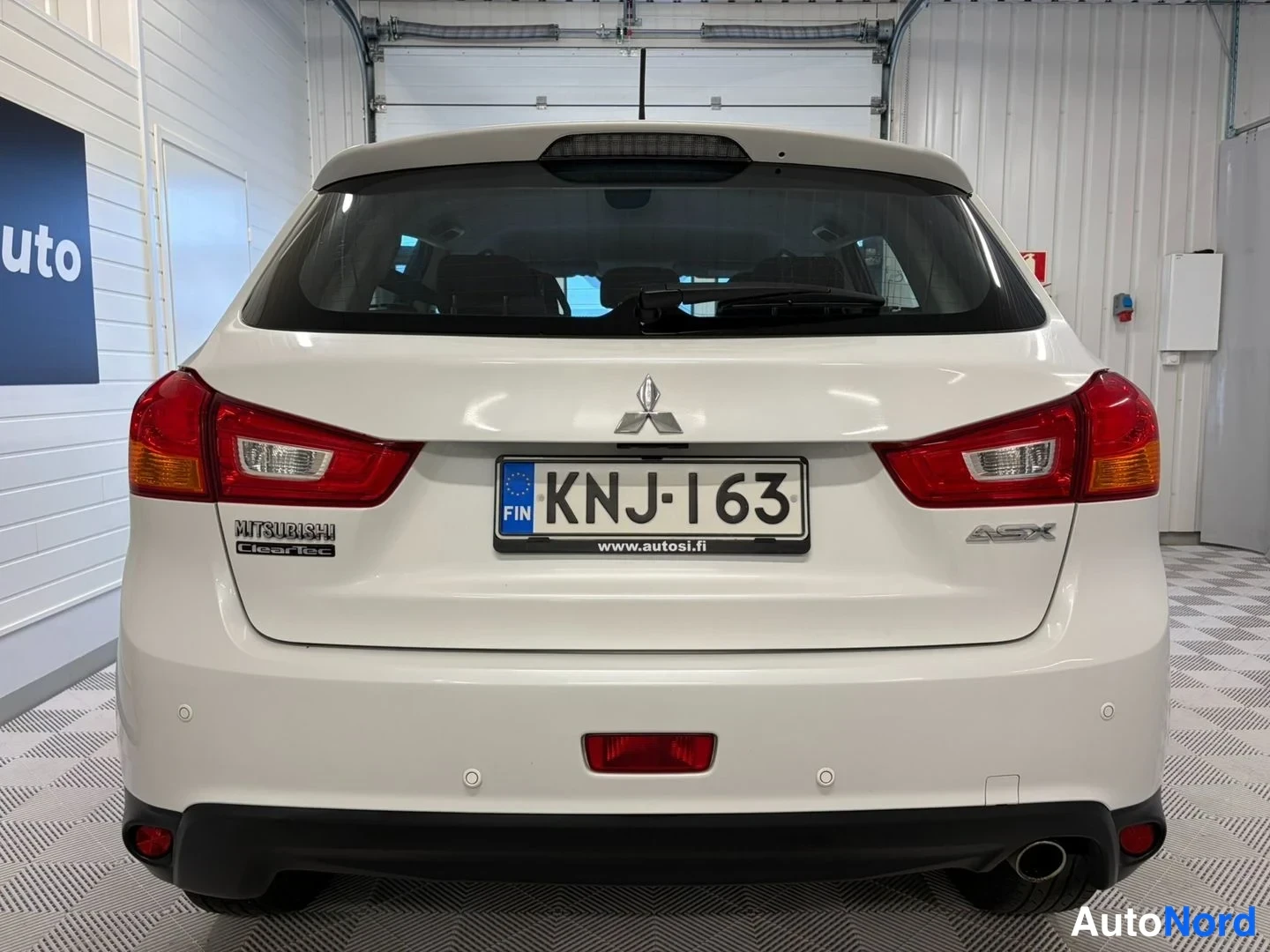 Takaa: Valkoisen Mitsubishi ASX:n takaosa suoraan takaa kuvattuna hallissa; rekisterikilpi, Mitsubishi- ja ASX-merkit näkyvät.