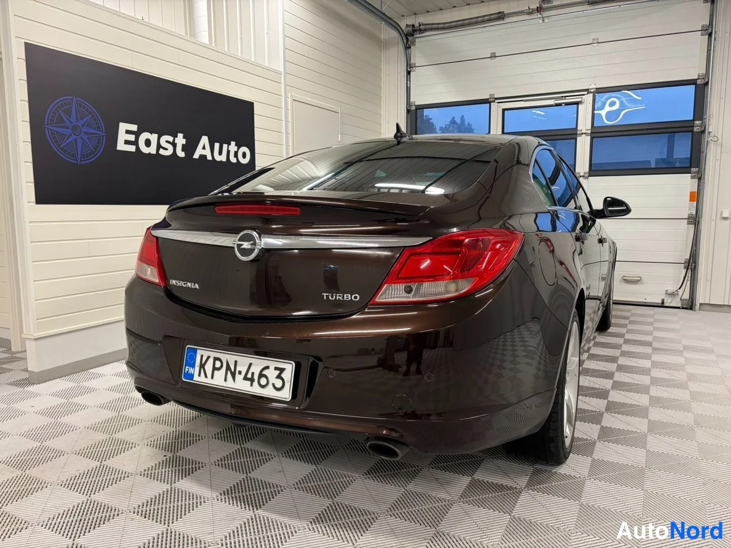 Takaviisto: Auton takapää ja vasen sivu kuvattuna kolmesta neljäsosasta: Opel Insignia, tummanruskea maali, rekisterikilpi, TURBO-teksti ja merkki takaluukussa.