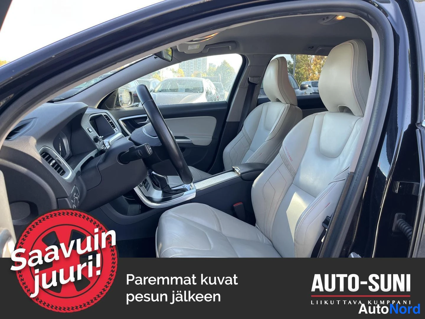 Sivulta: Auton etupenkki ja ohjaamo sisäapäin kuvattuna; vaaleat nahkapenkit, ohjauspyörä ja kojelauta näkyvät.