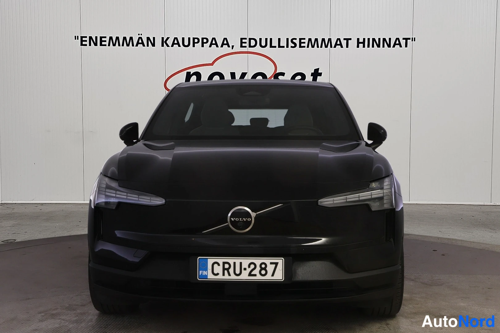 Edestä: Mustan auton etunäkymä; VOLVO-merkki ja rekisterikilpi näkyvät.