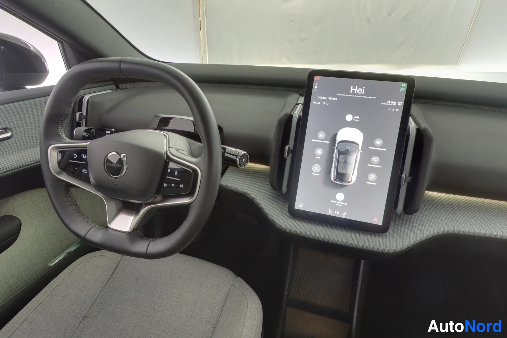 Muu: Auton sisätilat kuljettajan puolelta; VOLVO-ohjauspyörä ja kosketusruutu, jossa teksti Hei.