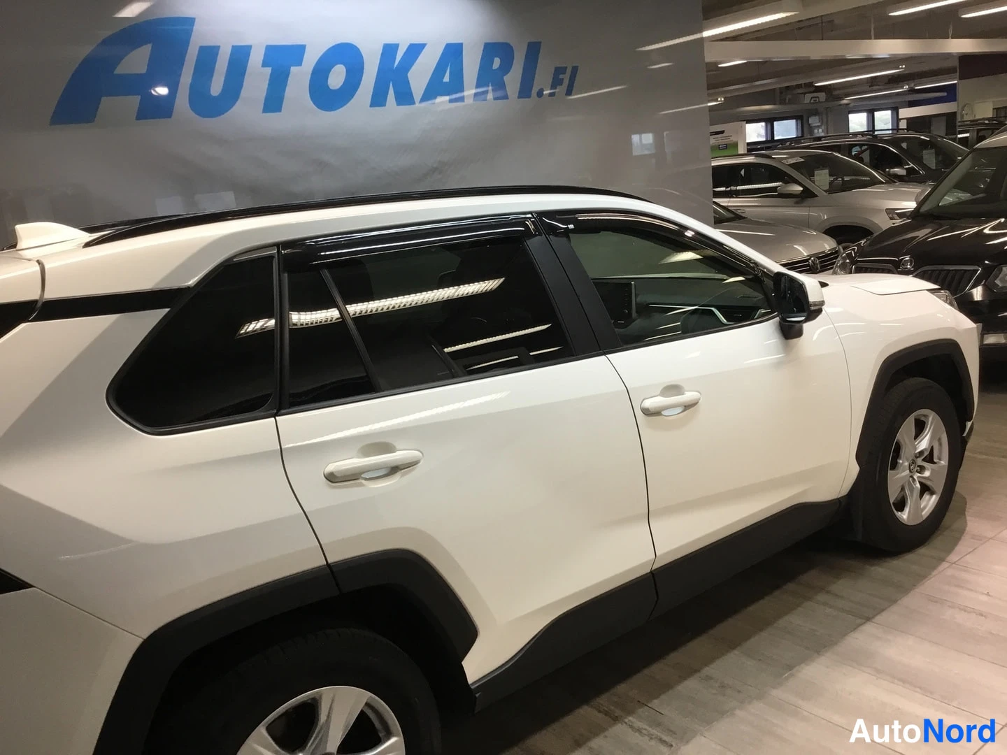 Sivulta: Valkoisen Toyota RAV4:n sivunäkymä oikealta puolelta; ovenkahvat, tummat ikkunat ja silver-vanteet näkyvät sisätiloissa.