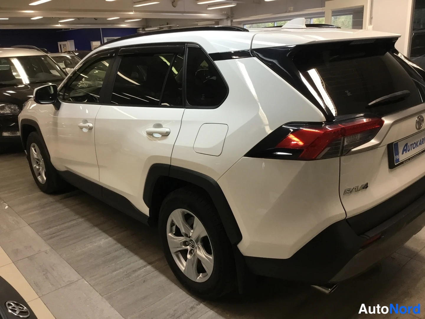 Takaviisto: Valkoisen Toyota RAV4:n takakulmanäkymä; takavalot, RAV4-merkki ja Autokari-tunniste näkyvät, kylki vasemmalla.