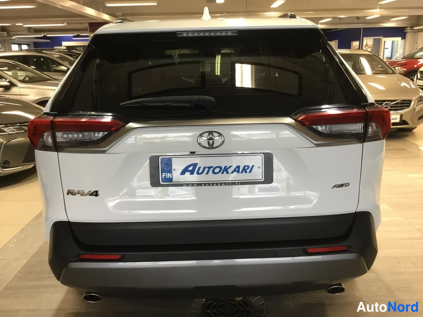 Takaa: Toyotan takapää takaa: valkoinen kannen ja puskurin alue, RAV4-merkki, Toyota-merkki, Autokari-kilpi ja AWD-merkki.