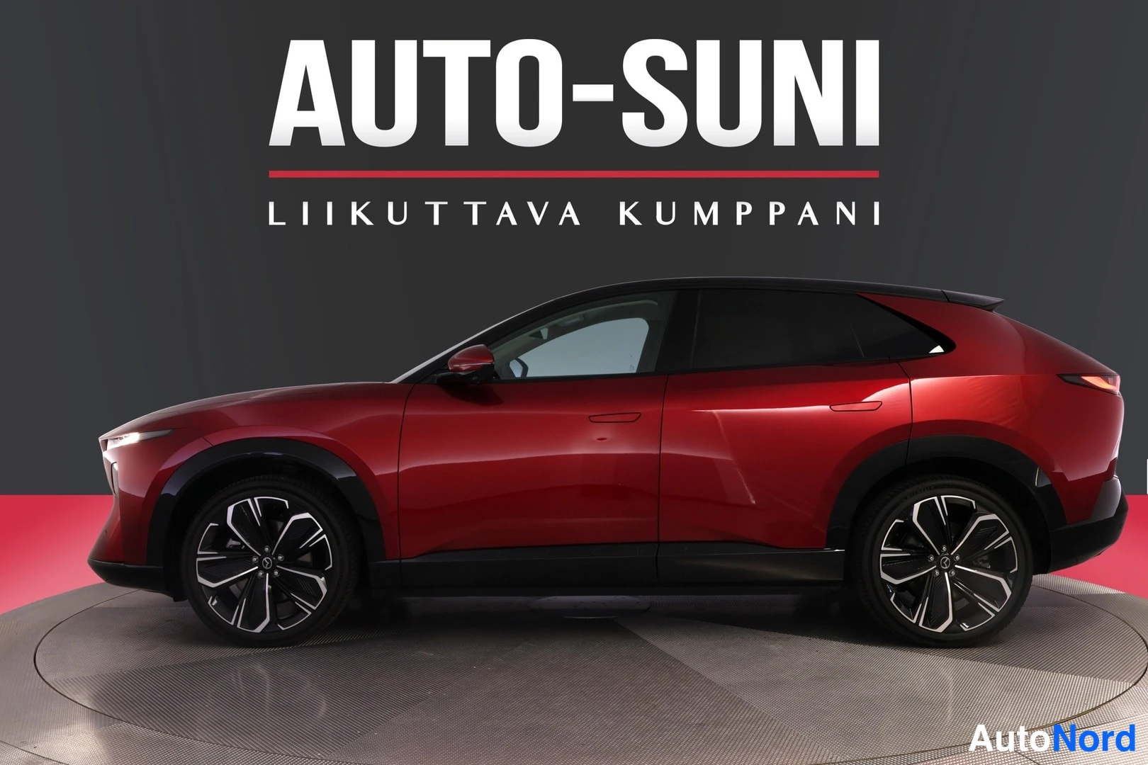 Sivulta: Punainen Mazda CX-6e -auto sivusta kuvattuna, mustat pyöränkaaret ja ilmastointigrillit näkyvissä.