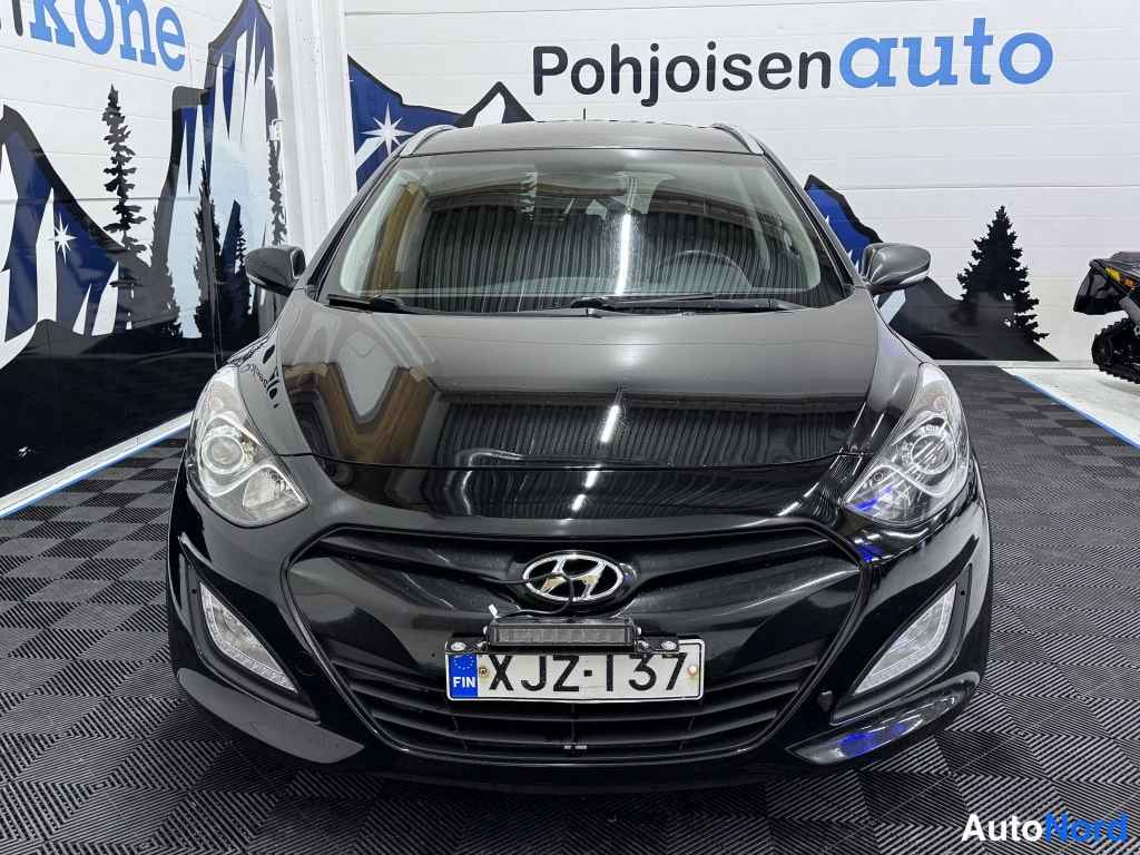 Edestä: Mustan Hyundai i30 -auton suora edustanäkymä, rekisterikilpi, Hyundai-logo näkyy, takana Pohjoisauto-mainostaulu.