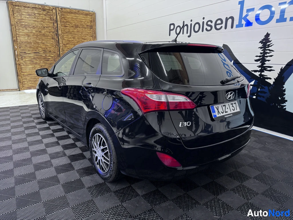 Takaviisto: Mustan Hyundai i30 -farmarin takakulma sisätiloissa; takavalot, i30-merkintä ja rekisterikilpi näkyvät.