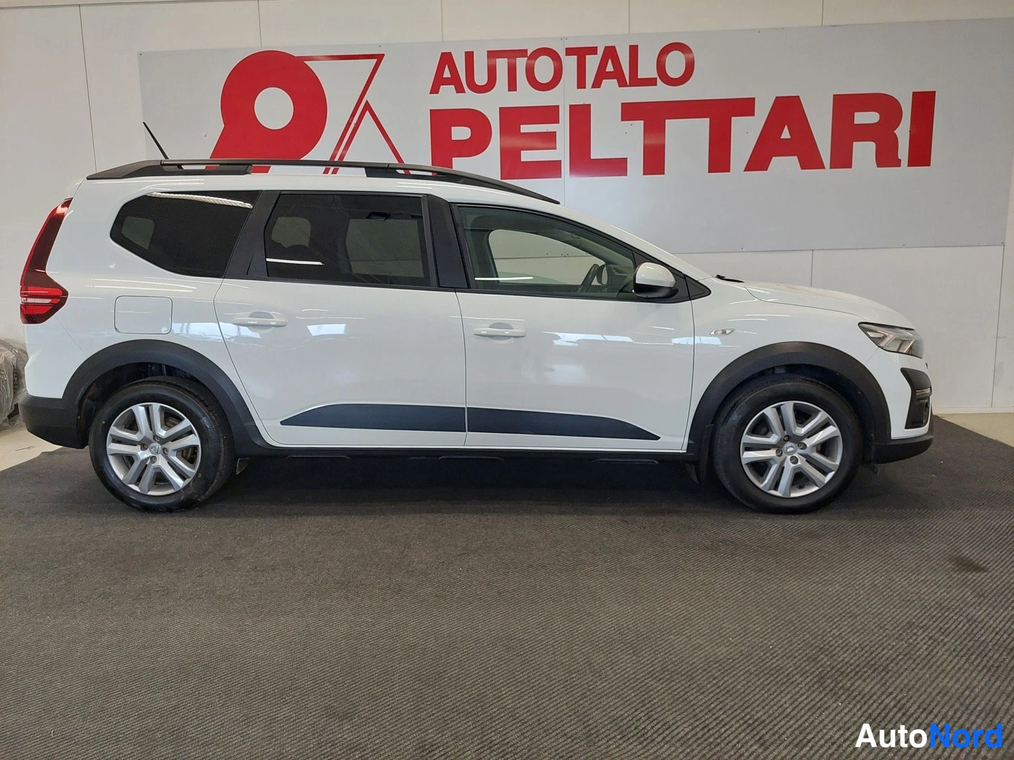 Etuviisto, nokka oikealle: Dacia Jogger -farmariauto sivulta hieman edestä kuvattuna; valkoinen koripaneli, mustat ikkunakehykset ja kattotankoa ei näy kokonaan.