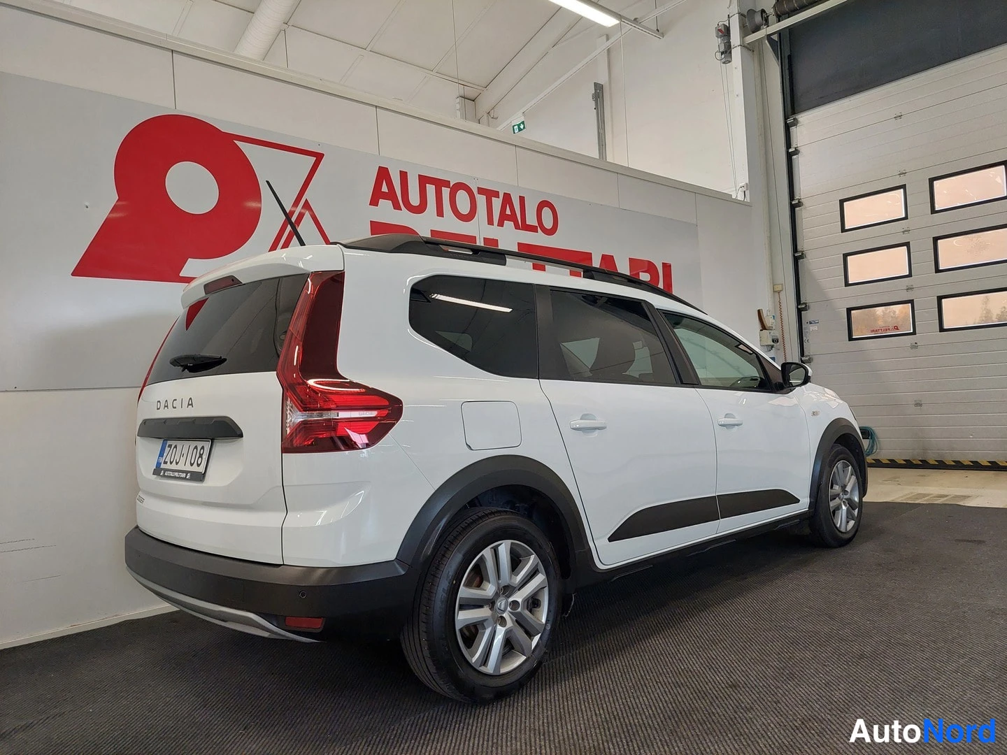 Takaviisto: Dacia Jogger takaviistosta: valkoinen koripaneeli, katolla kattokaiteet, takana DACIA-teksti ja kilpi.