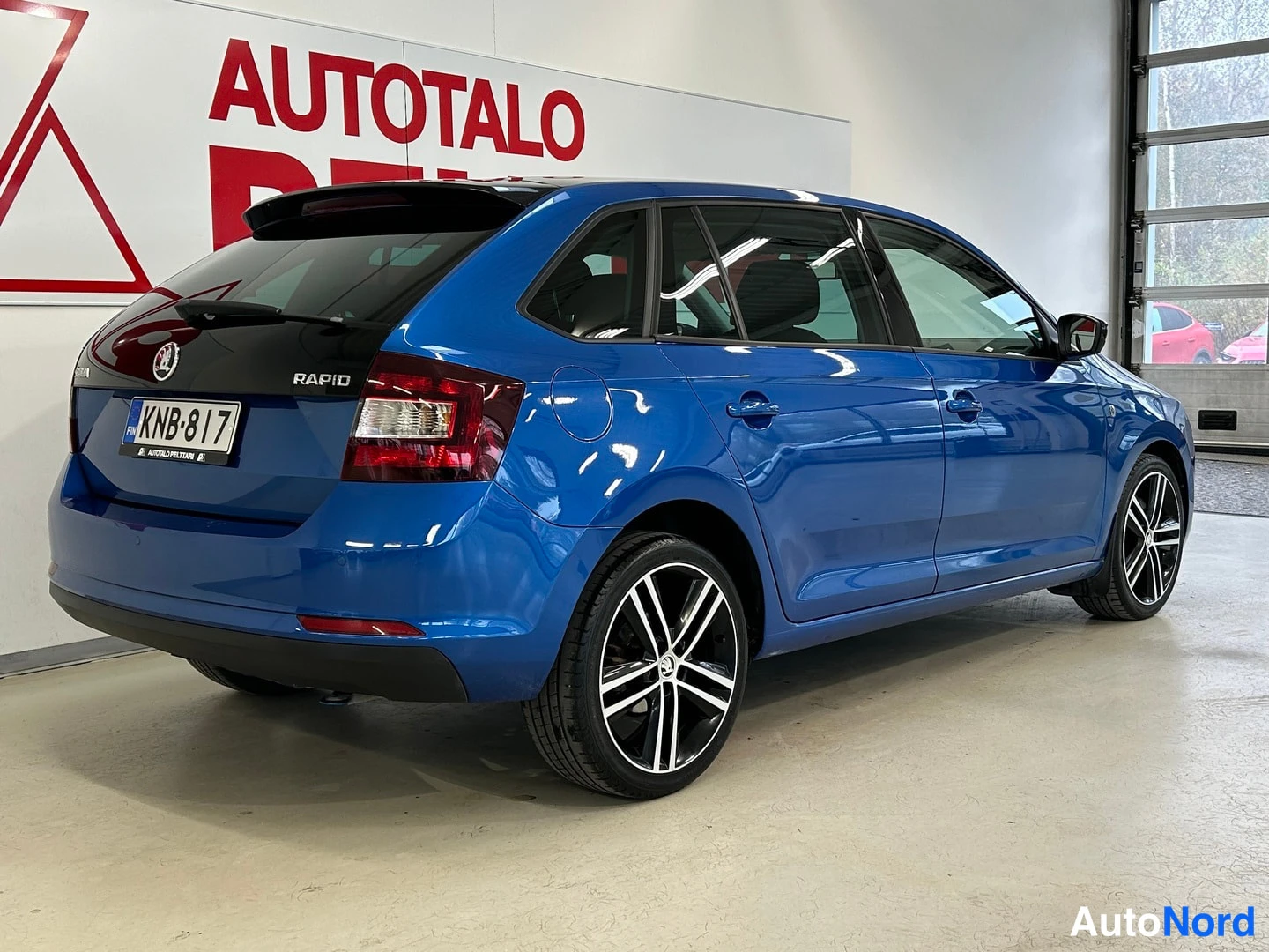 Takaviisto: Sininen Skoda Rapid takaa ja oikealta sivulta kuvattunaAutotalo Peltarin sisätiloissa, rekisterikilpi.