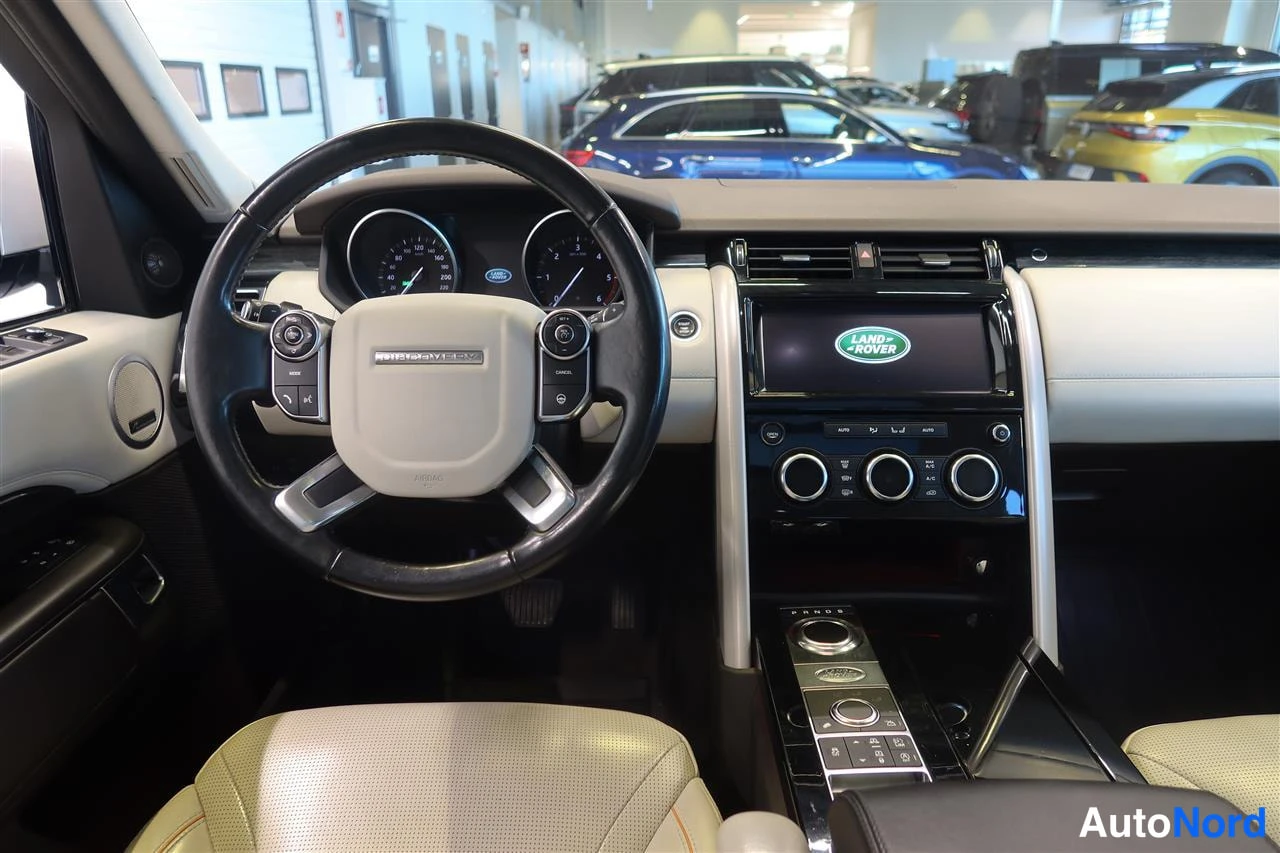 Sivulta: Ohjaamo näkyy kuljettajan puolelta: kaksivärinen ohjauspyörä, mittaristo ja Land Rover -multimedia näyttö keskikonsolissa.
