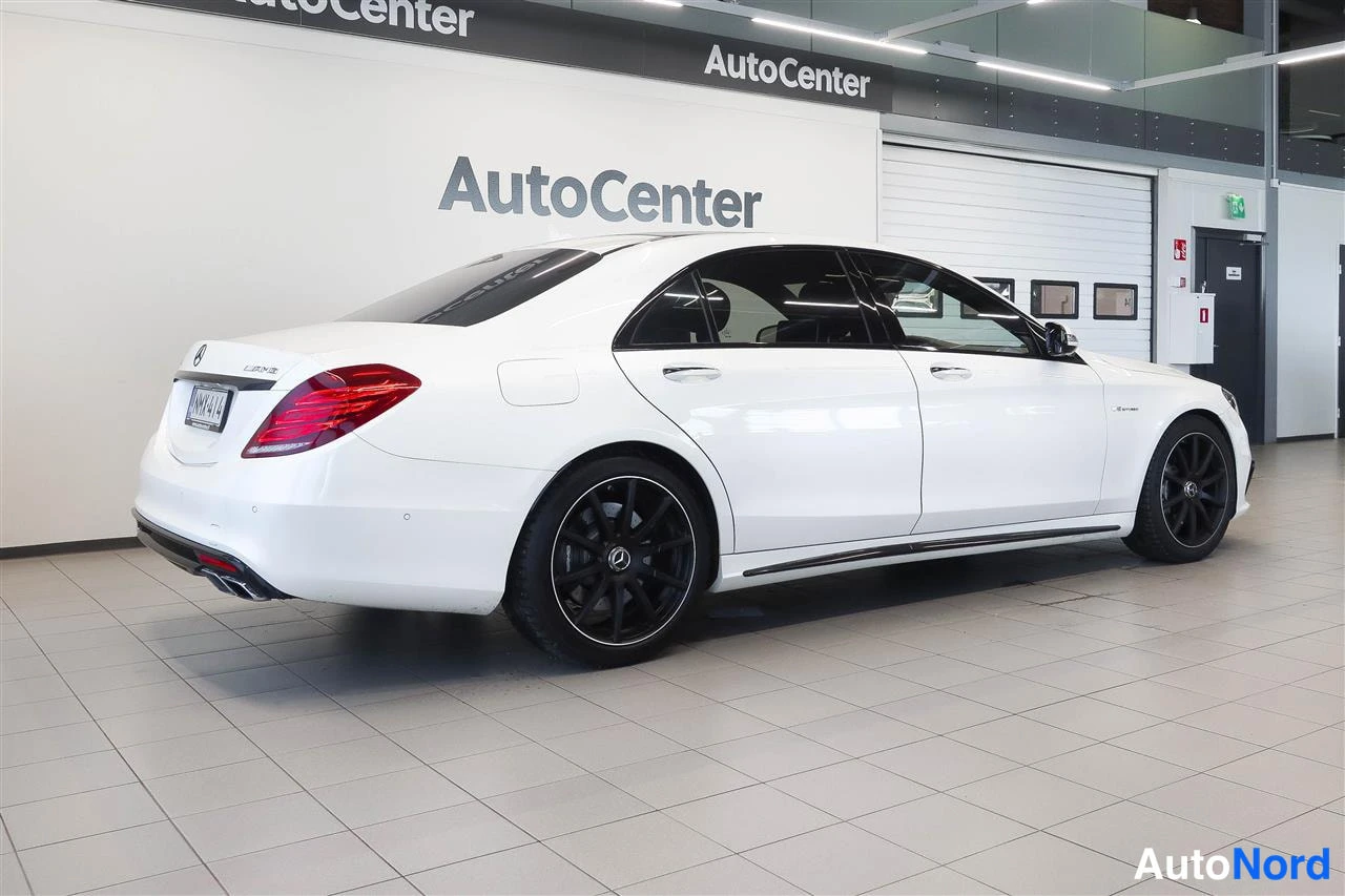 Takaviisto: Valkoinen Mercedes-Benz S-luokan sedan takaa sivulta kuvattuna tyhjässä AutoCenter-hallissa.