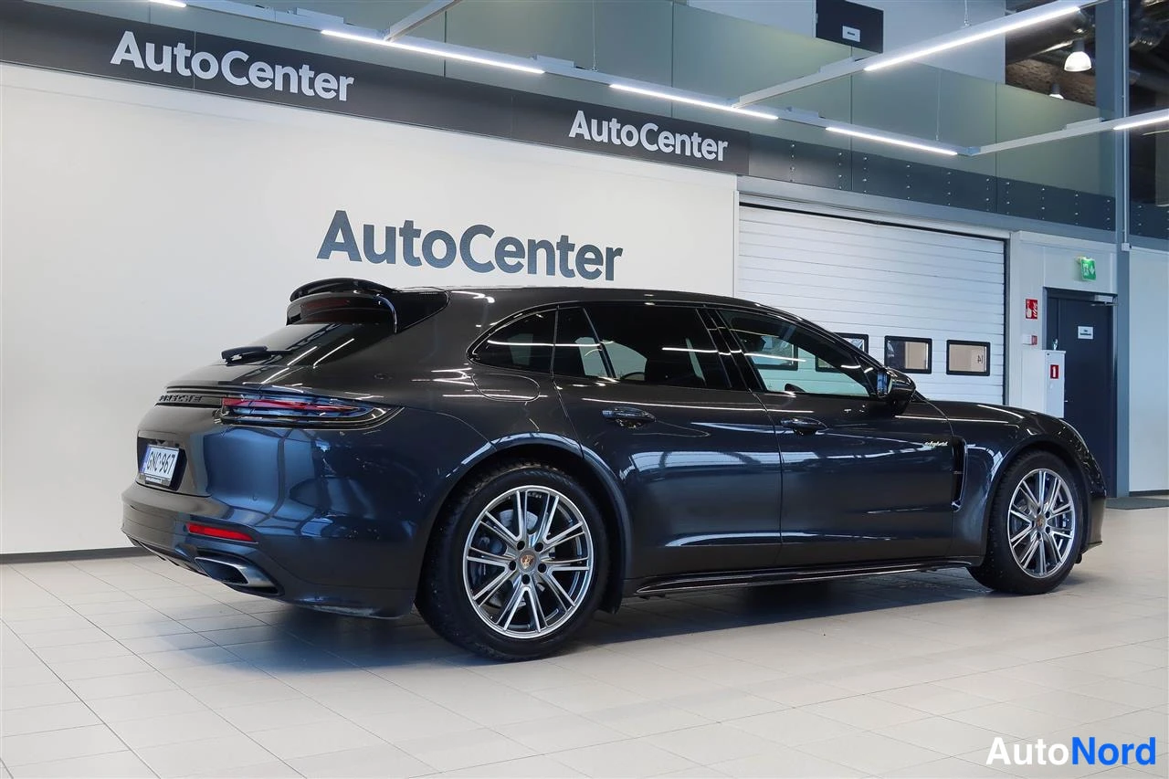 Takaviisto: Tummanharmaan Porsche Panamera Sport Turismon takakulma autonäyttelytilassa
