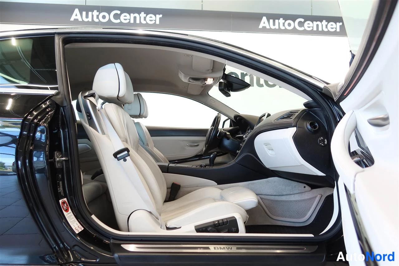 Muu: Kaksipaikkainen sisätilan näkymä, valkoiset istuimet ja BMW-korimerkki kynnyksellä, ovista kuvattuna.
