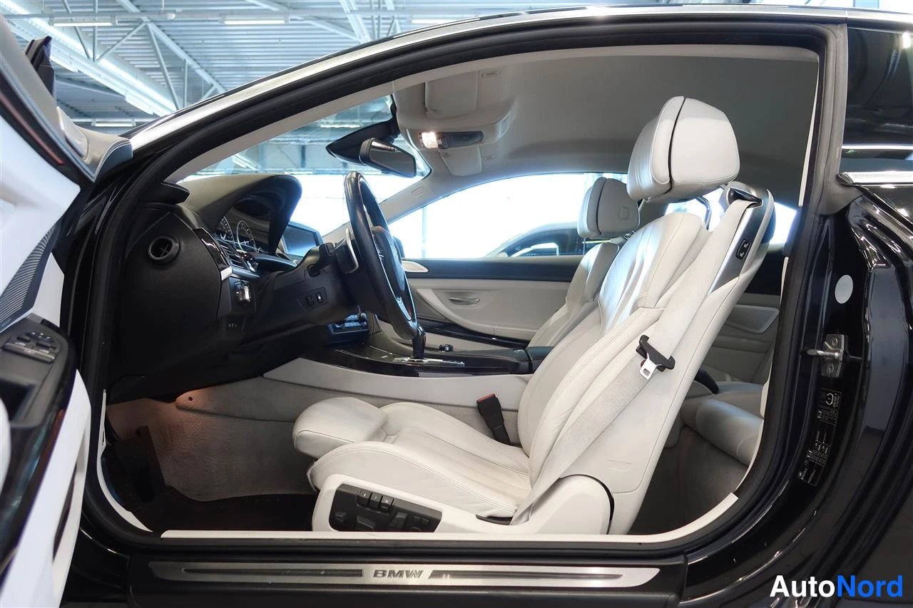 Muu: Auton avattu kuljettajan ovi ja ohjaamo: vaaleat nahkaistuimet, ohjauspyörä ja olokynnyksellä BMW-teksti.