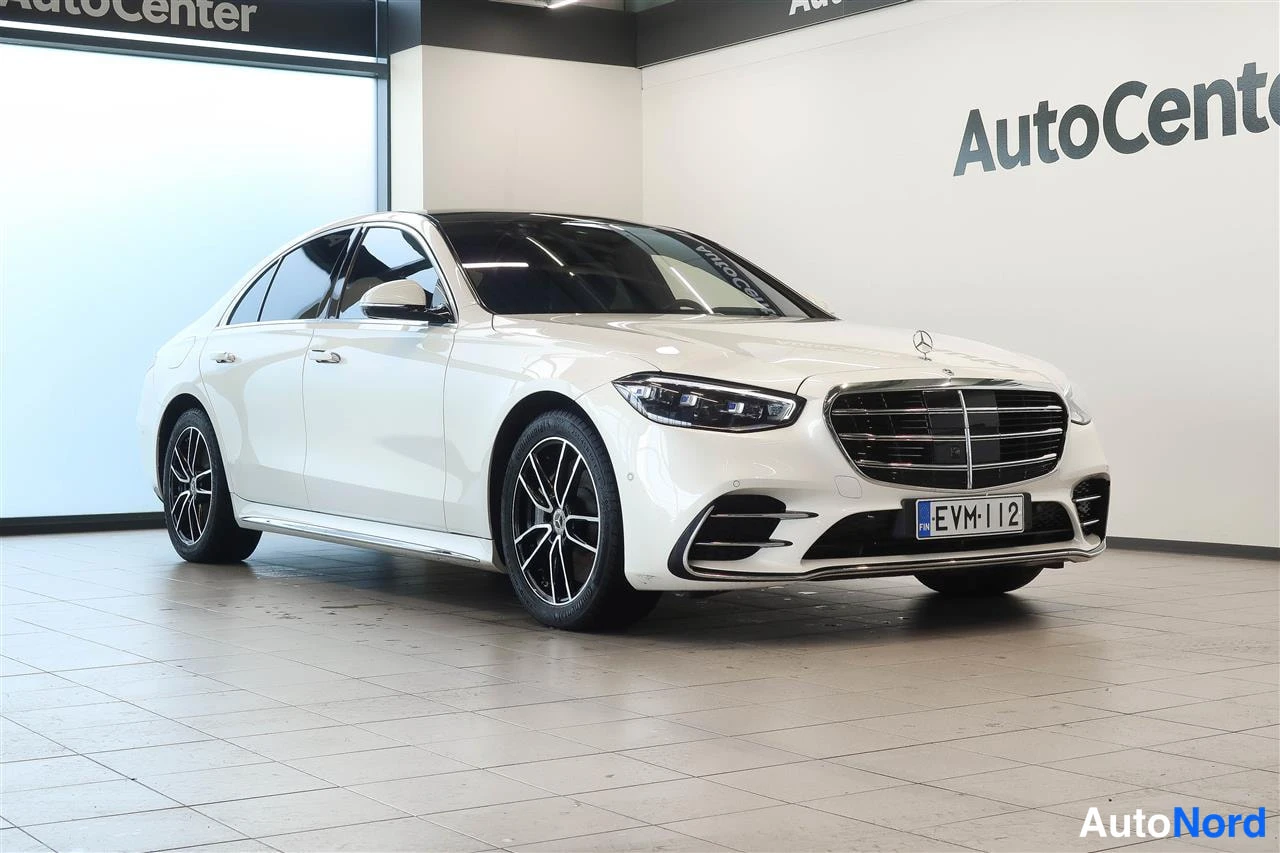 Etuviisto, nokka oikealle: Valkoinen Mercedes-Benz S-sedan etukulmasta oikealta nähtynä sisätiloissa, rekisteritunnus.