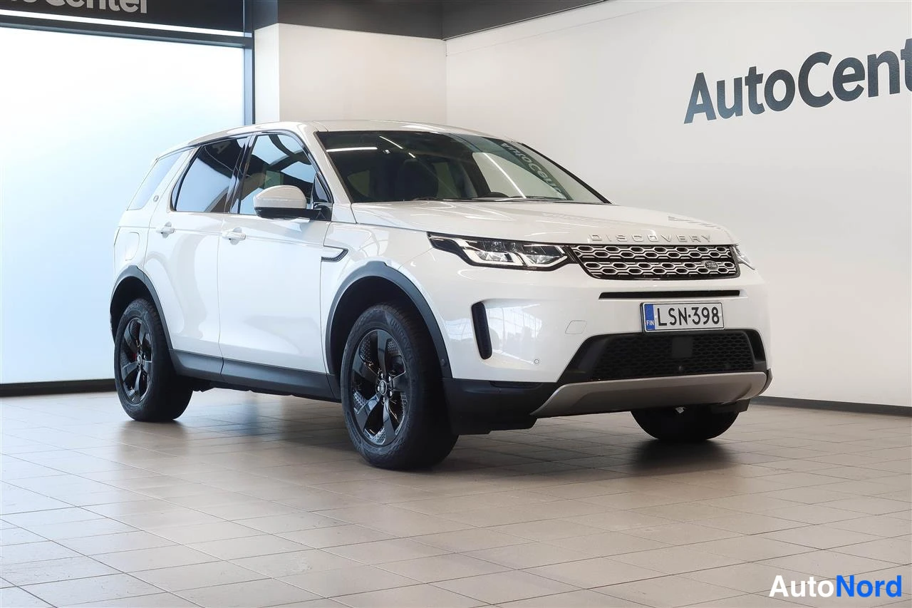 Etuviisto, nokka oikealle: Land Rover Discovery Sport -maastauto etukulmasta, nokka oikealle, valkoinen kori, mustat vanteet ja hienostuneet ohjaustehostevat pyörät, rekisterikilpi