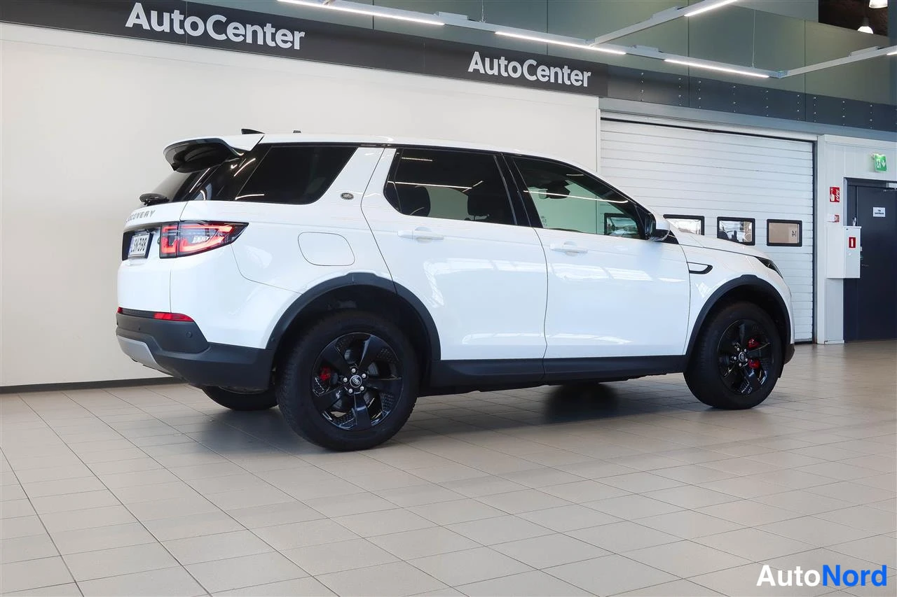 Takaviisto: Valkoisen farmari-SUV:n takakulmanäkymä sisätiloissa, mustat vanteet ja takavalo näkyvät.