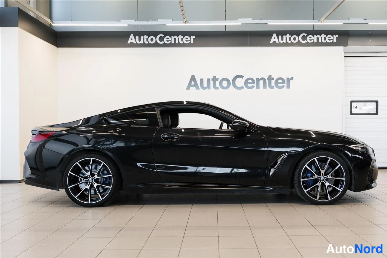 Sivulta: BMW 840 -kupé sivulta oikealta vasemmalle kuvattuna autosalonissa, musta runko ja monihaaraiset kevytmetallivanteet.