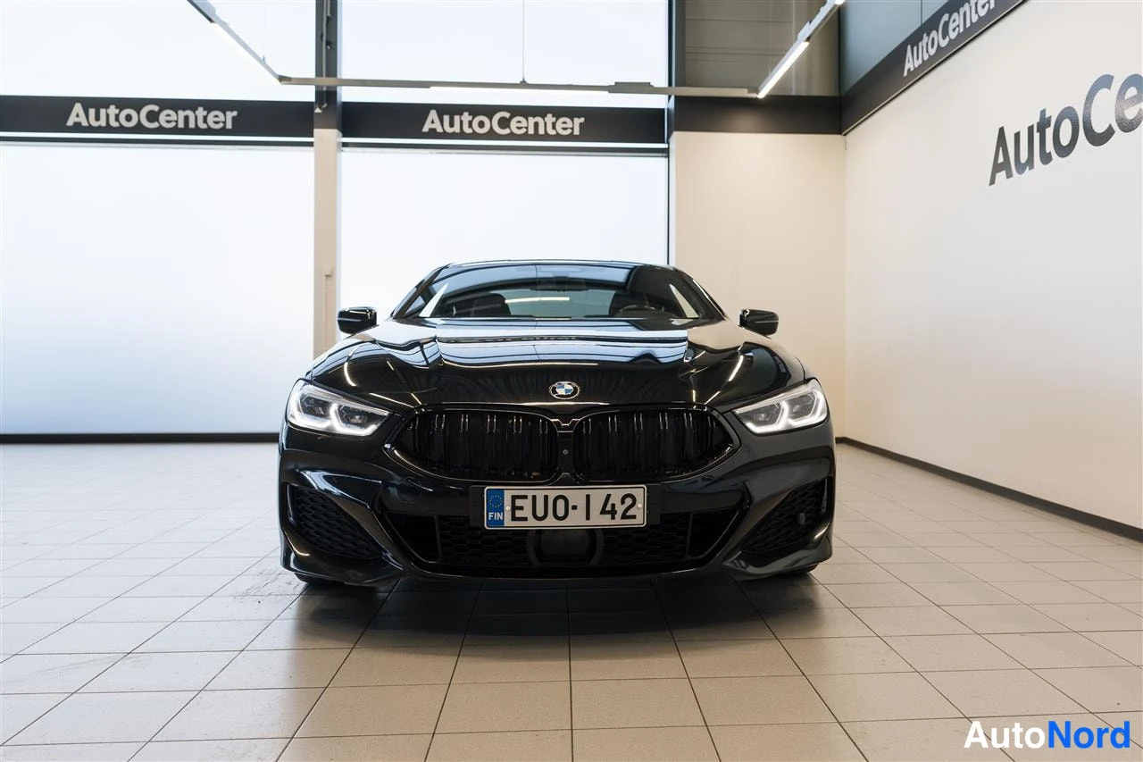 Edestä: BMW 840 -kupé suoraan edestäpäin autosalonissa, mustat etusäleikkö ja puskuri, rekisterikilpi EU0-142.
