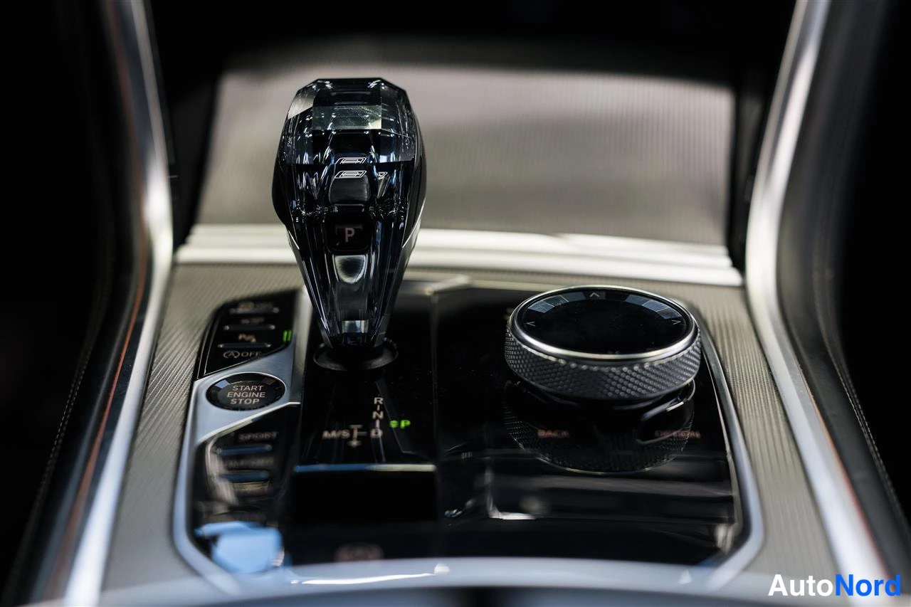 Yksityiskohta: Auton keskikäyttöpaneeli lähikuvassa: automaattivaihteen valitsin, START ENGINE STOP -painike ja iDrive-säädin.