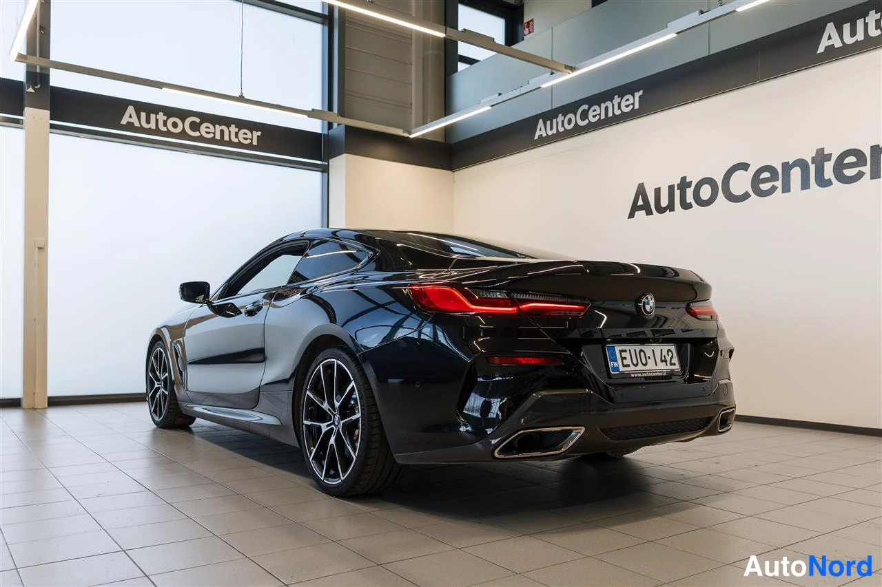 Takaviisto: Musta coupé takaa kulmasta kuvattuna AutoCenter-hallissa; takavalot, perävaunu ja rekisterikilpi näkyvät.