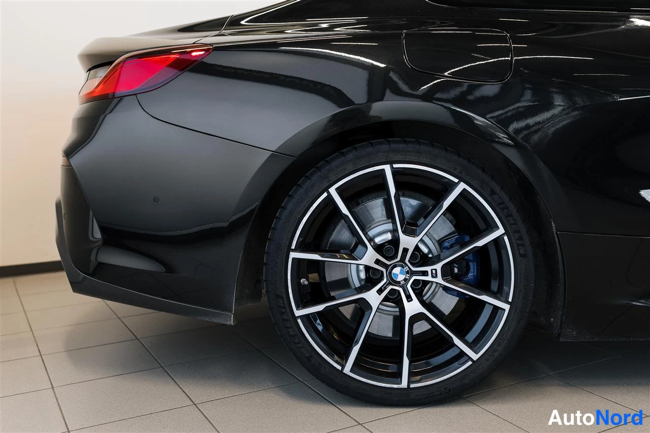 Takaviisto: Mustan auton takakulma ja takavyöry, BMW-merkkinen kaivotyylinen vannes informaatio.