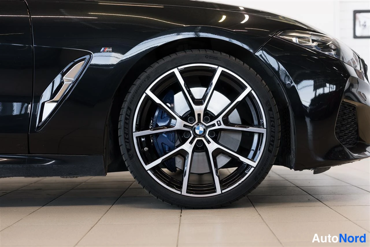 Etuviisto, nokka oikealle: Mustan BMW:n etupyörän lähikuva: kaksivärinen kevytmetallivanne, Michelin-rengas ja sininen levyjarrusatula.