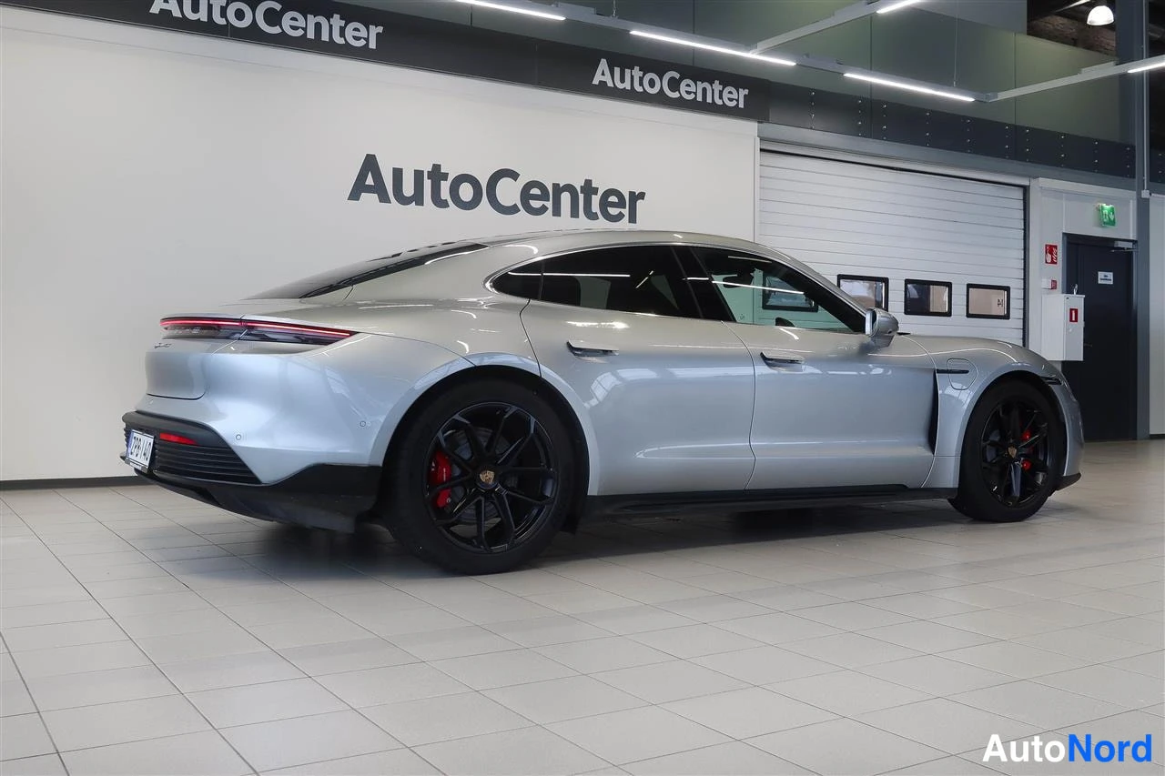 Takaviisto: Hopeanvärinen Porsche Taycan -auton takakulma kylki näkyvissä sisätiloissa; takavalojenabort ja mustat vanteet punaisilla jarrusatuloilla näkyvät.