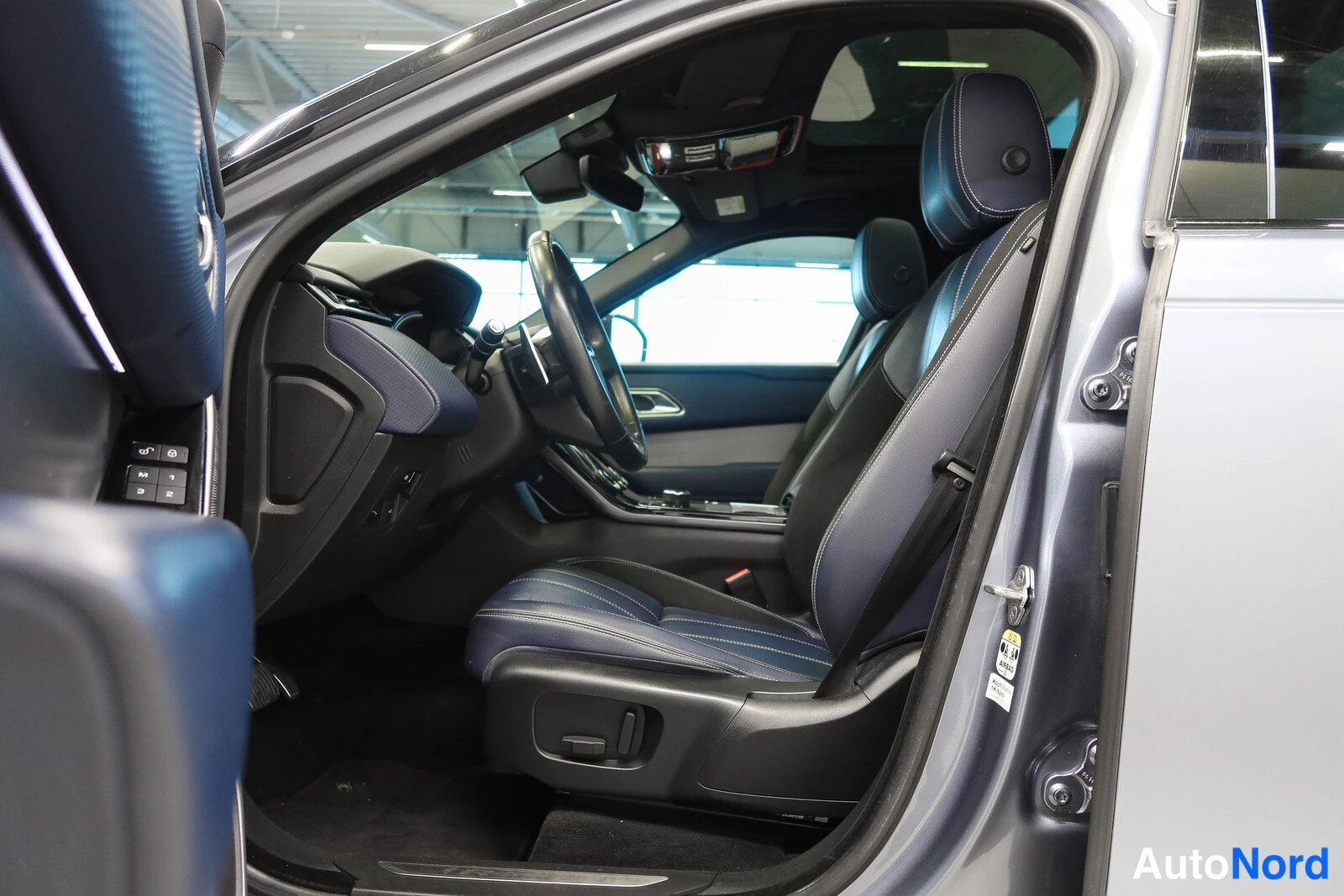 Muu: Auton etuistuimet ja ohjaamo avatusta ovesta kuvattuna; tummansiniset nahkapenkit, ohjauspyörä ja panoraamakatto näkyvät.