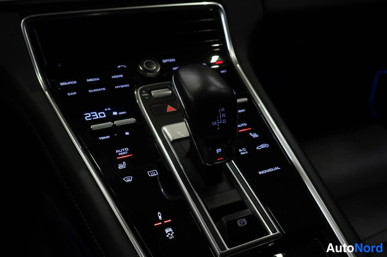 Muu: Auton automaattivaihteen valitsin ja sitä ympäröivät nappien ohjauspaneelit pimeässä ohjaamossa; lämpötila näkyy 23,0 astetta.