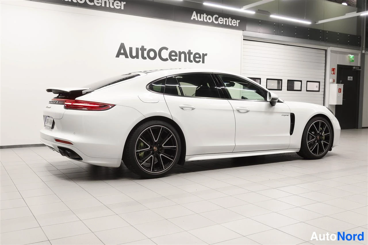 Takaviisto: Valkoinen Porsche Panamera takaviistosta AutoCenter-hallissa, rekisterikilpi ja dual twin pipe -takapuskuri näkyvät.