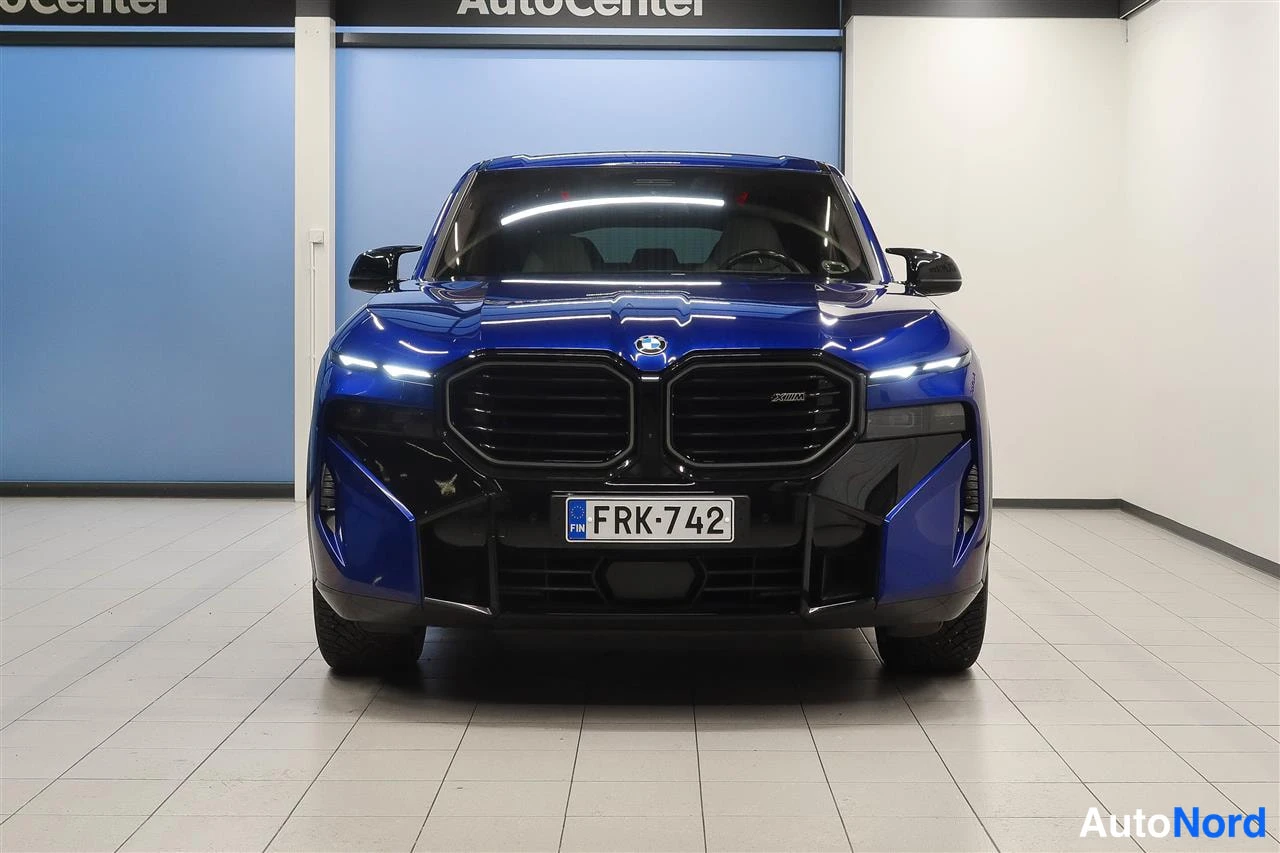 Edestä: Sininen BMW XM suoraan edestä, suuret munuaiset ja ohut DRL-valot, rekisterikilpi.