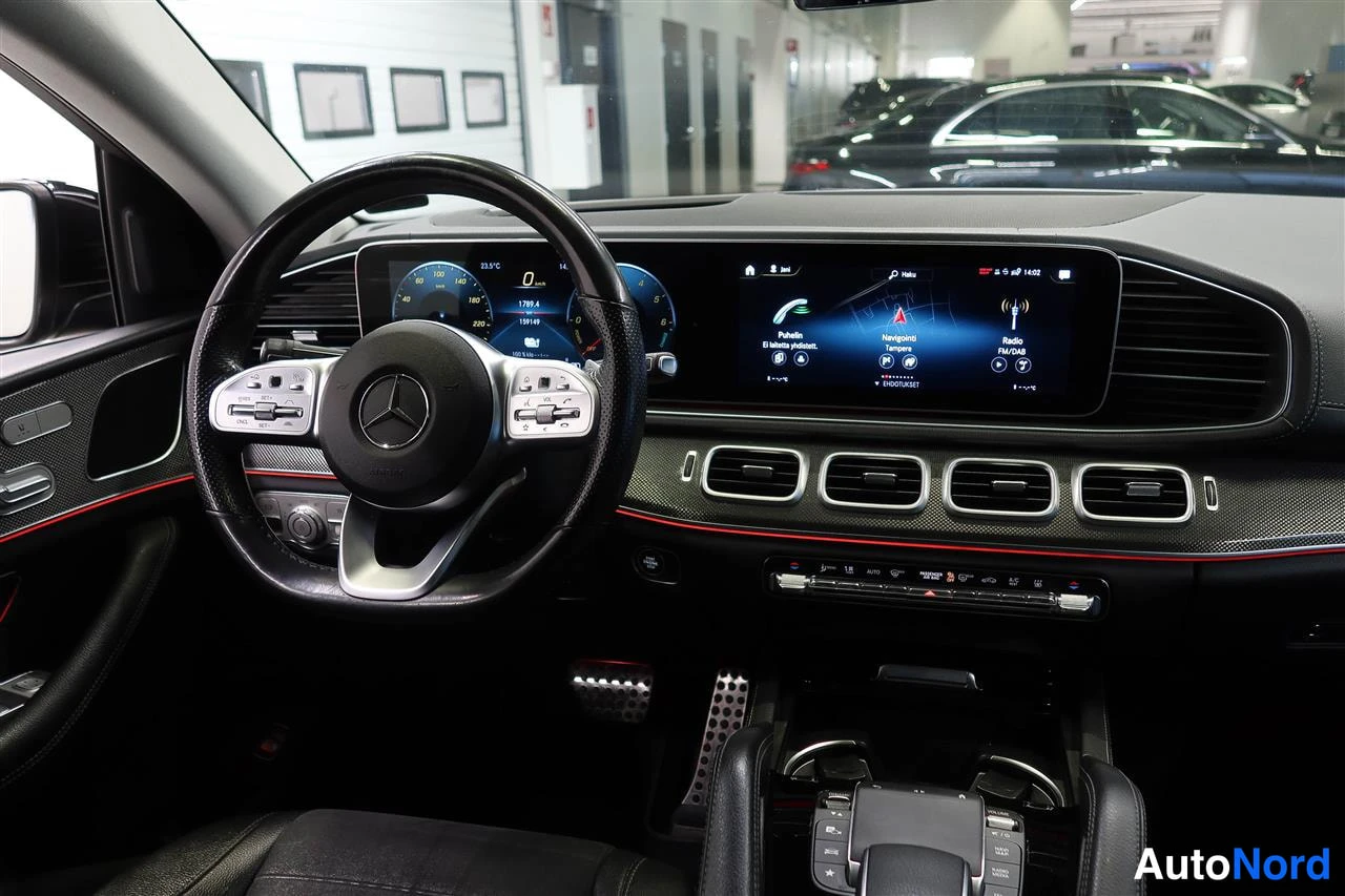 Muu: Kuljettajan näkymä: Mercedes-ohjauspyörä, digitaalinen mittaristo ja infotainment-näyttö navikka- ja radioläheillä, punaiset korostusviivat.