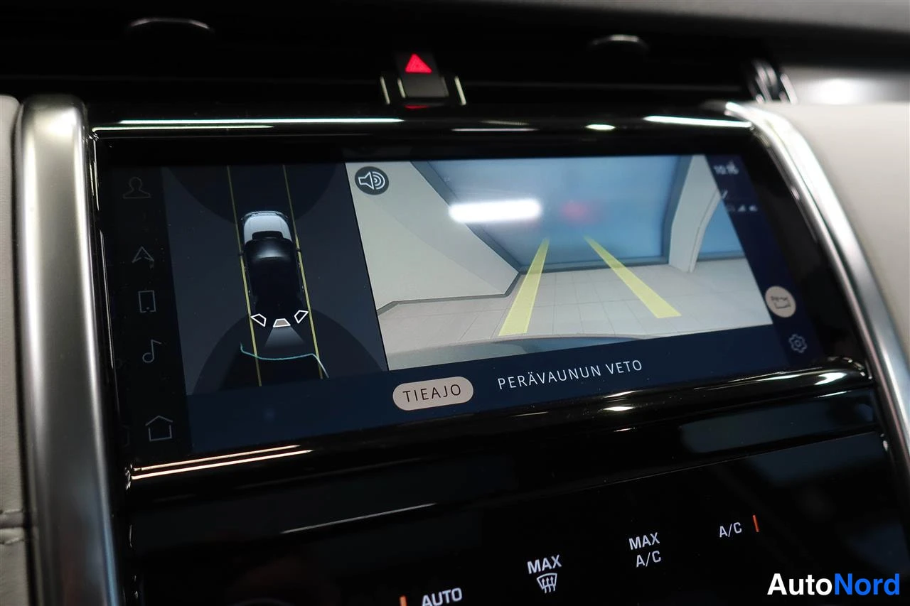 Edestä: Täyttä näyttöä näkyy: infotainment-näyttö näyttää peruutus kameran kuvan ja huomaa tekstin 'PERÄVAUNUN VETO' sekä napin 'TIEAJO'. Näkymä sisältää myös Max A/C j