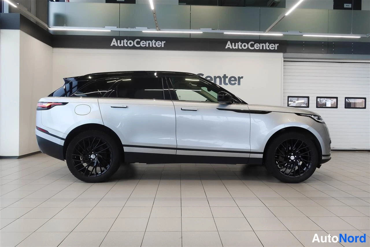Takaviisto: Hopeanvärinen Range Rover Velar takakulmasta kuvattuna sisätiloissa, mustat vanteet ja kontrastimustakatto.