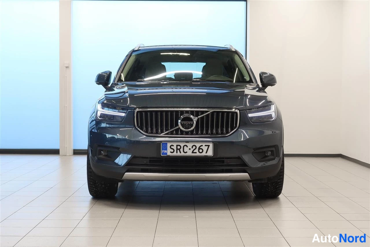 Edestä: Tummansininen Volvo XC40 suora etuulta kuvattuna sisätiloissa, Volvo-merkki säleikössä ja rekisterikilpi