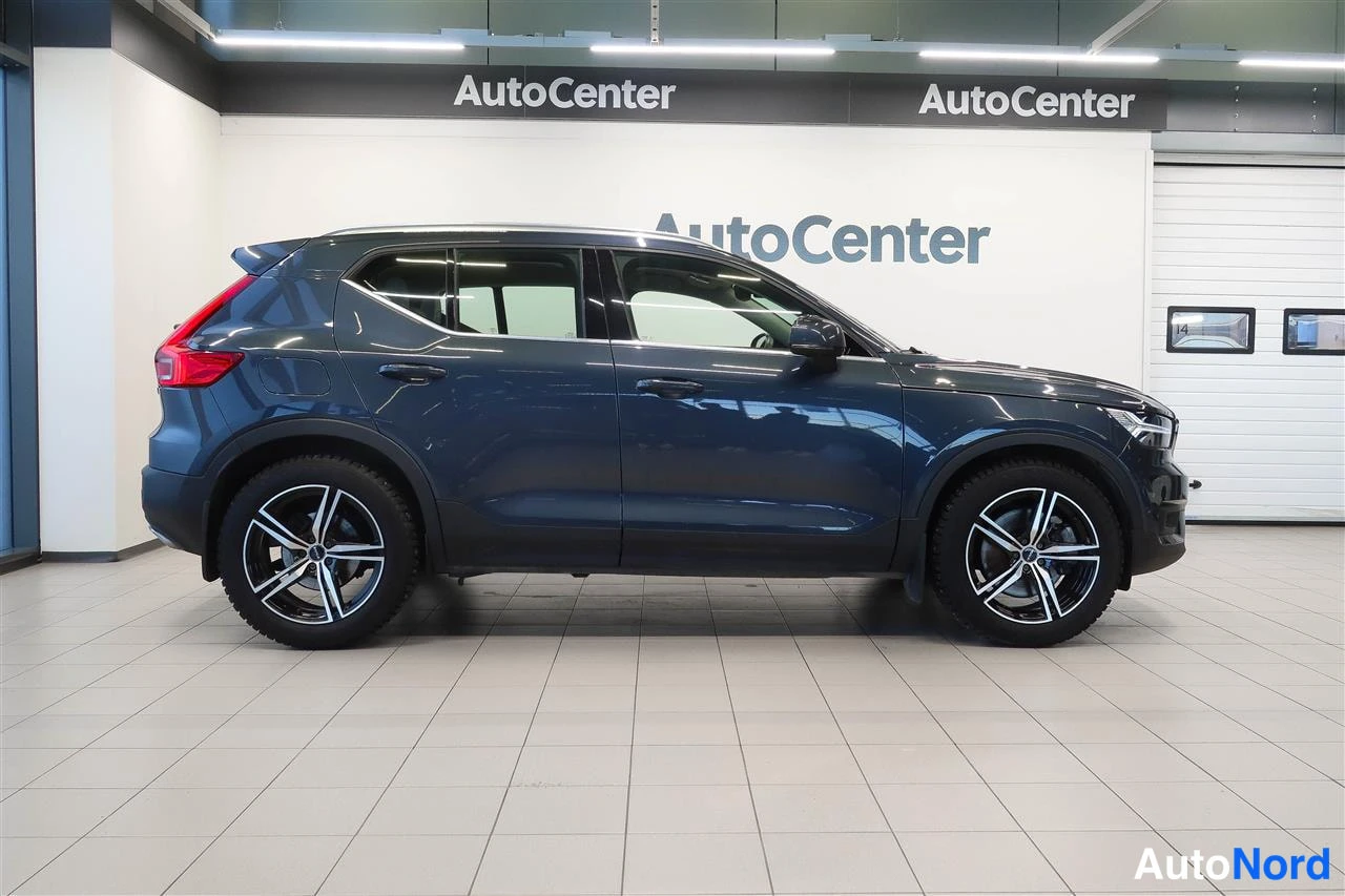 Takaviisto: Tummansininen Volvo XC40 sivuulta oikealta puolelta kuvattuna sisätiloissa, mustat alumiinivanteet