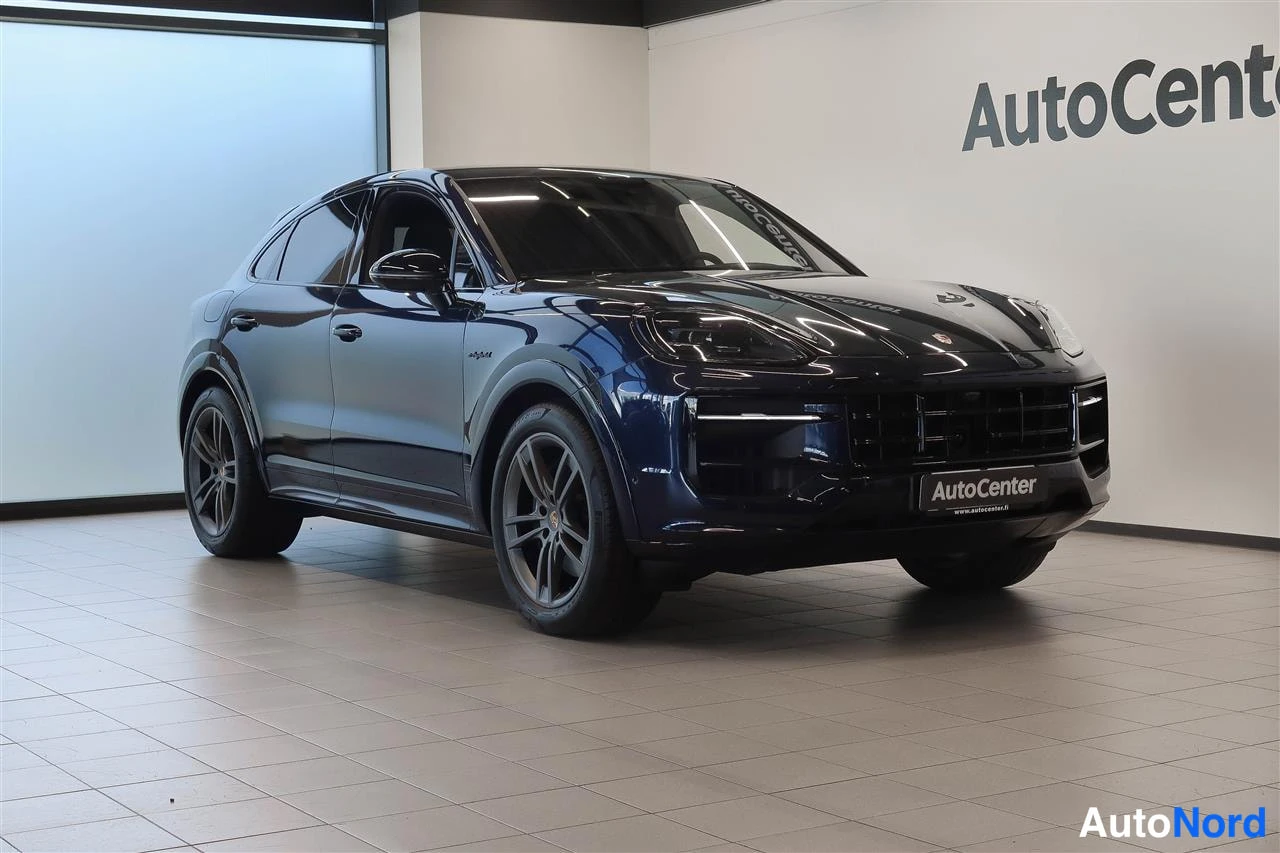 Etuviisto, nokka oikealle: Tummansininen SUV-etukulmakuva sisätiloissa; kylki ja etusäleikkö näkyvät, ja AutoCenter-teksti on näkyvissä taustaseinässä.